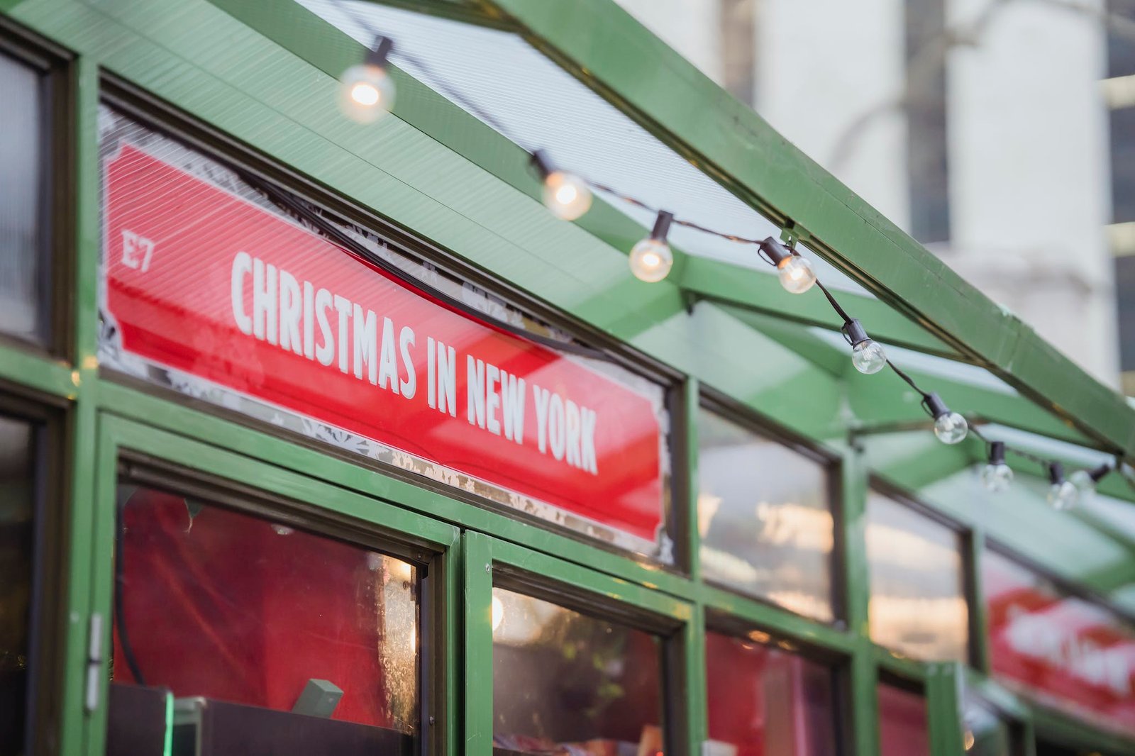 Low angle red signboard with Christmas In New York inscription hanging on glass showcase of shop on city street
